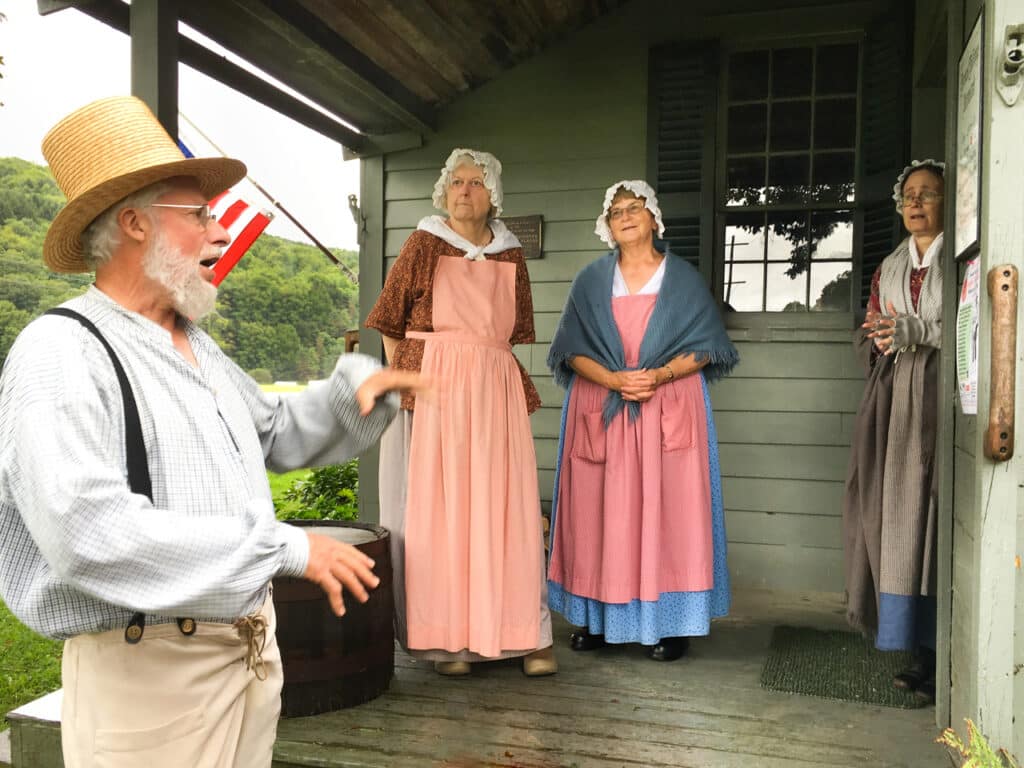 Four costumed interpreters leading a tour at a 19th century farmhouse museum. 
