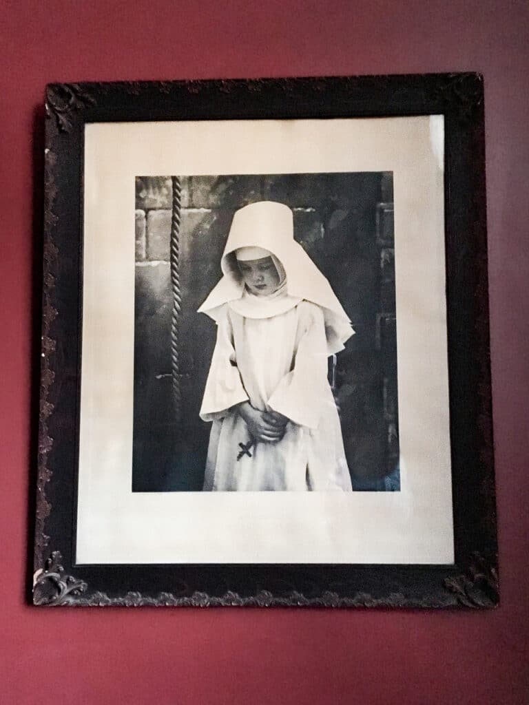 Spooky black and white photo of a child wearing a white nun's costume and holding a small crucifix.  