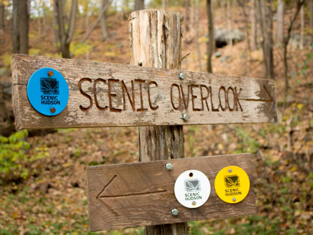 Wooden sign on a hiking trail, directing hikers to a scenic overlook.