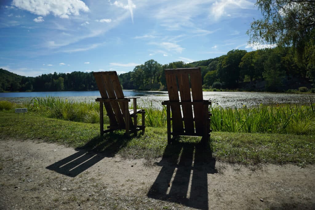Two wooden lounge chairs in front of a lake. 