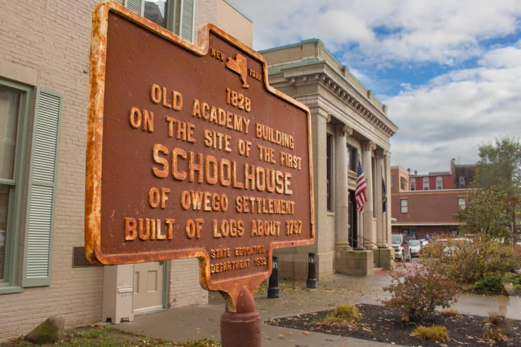 Historical marker in front of a building in Owego, NY, describing it as the site of a schoolhouse from 1828.