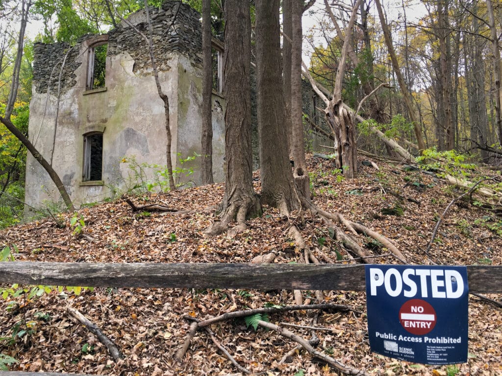A sign that says Posted-No Entry in front of ruins of a stone mansion in the woods. 