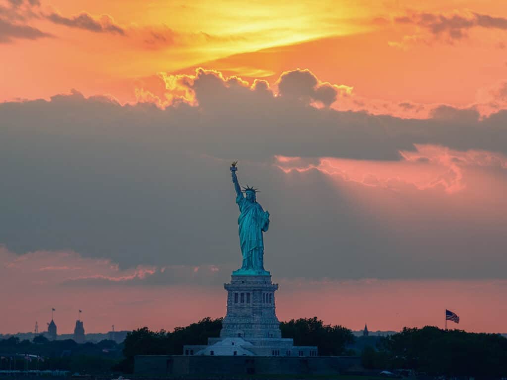 The Statue of Liberty against a colorful pink and orange sunset.