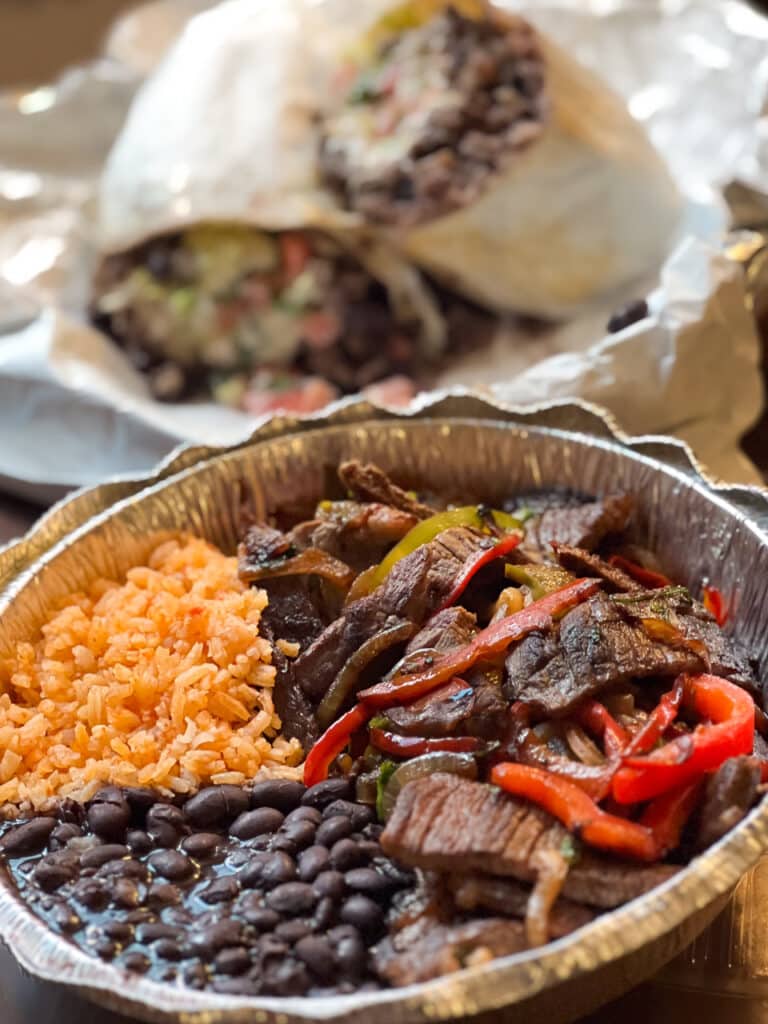 Steak fajitas with a side of rice and beans in an aluminum take-out container. 