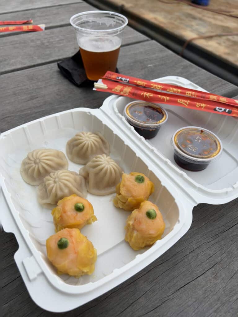 A serving of soup dumplings and shrimp shumai in an open plastic takeaway container. 