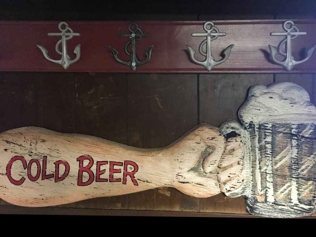 Worn painting of a man's muscular arm holding a beer. The words Cold Beer are in red on the arm. 