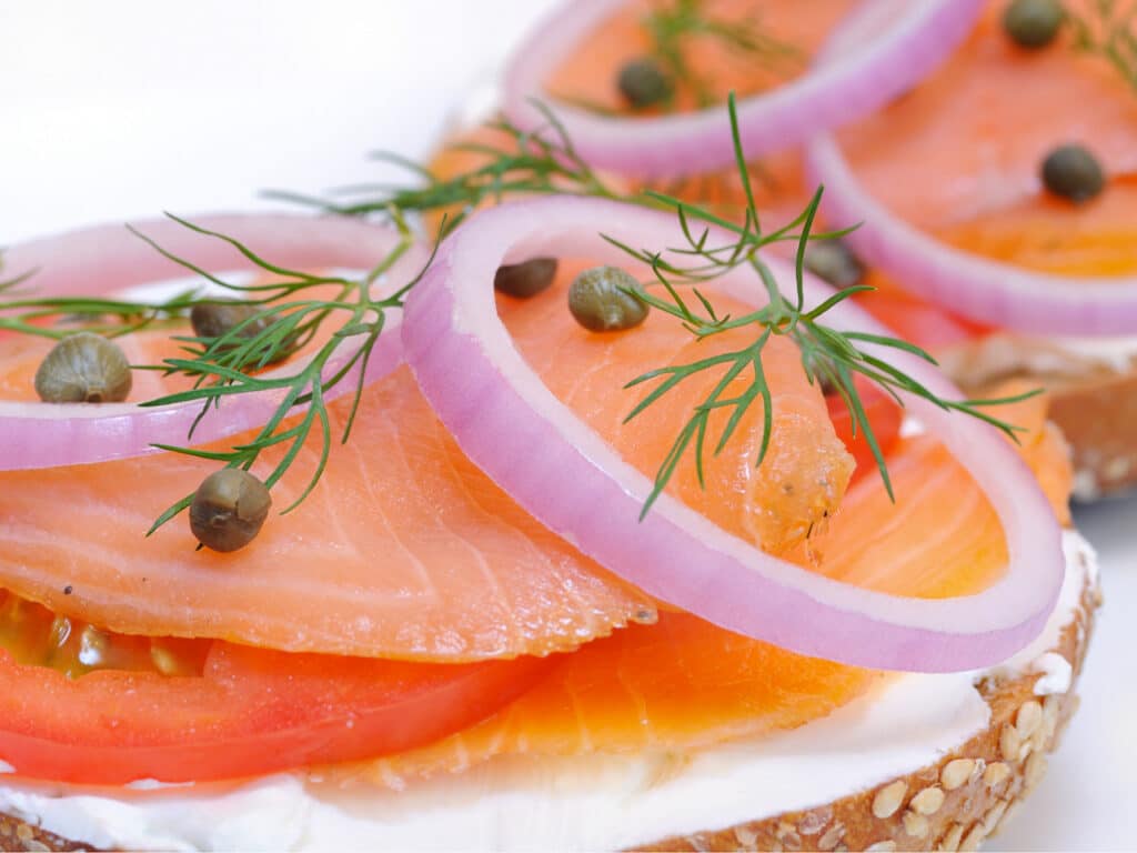 Close-up view of a lox and bagel sandwich, topped with capers, dill, and red onions.