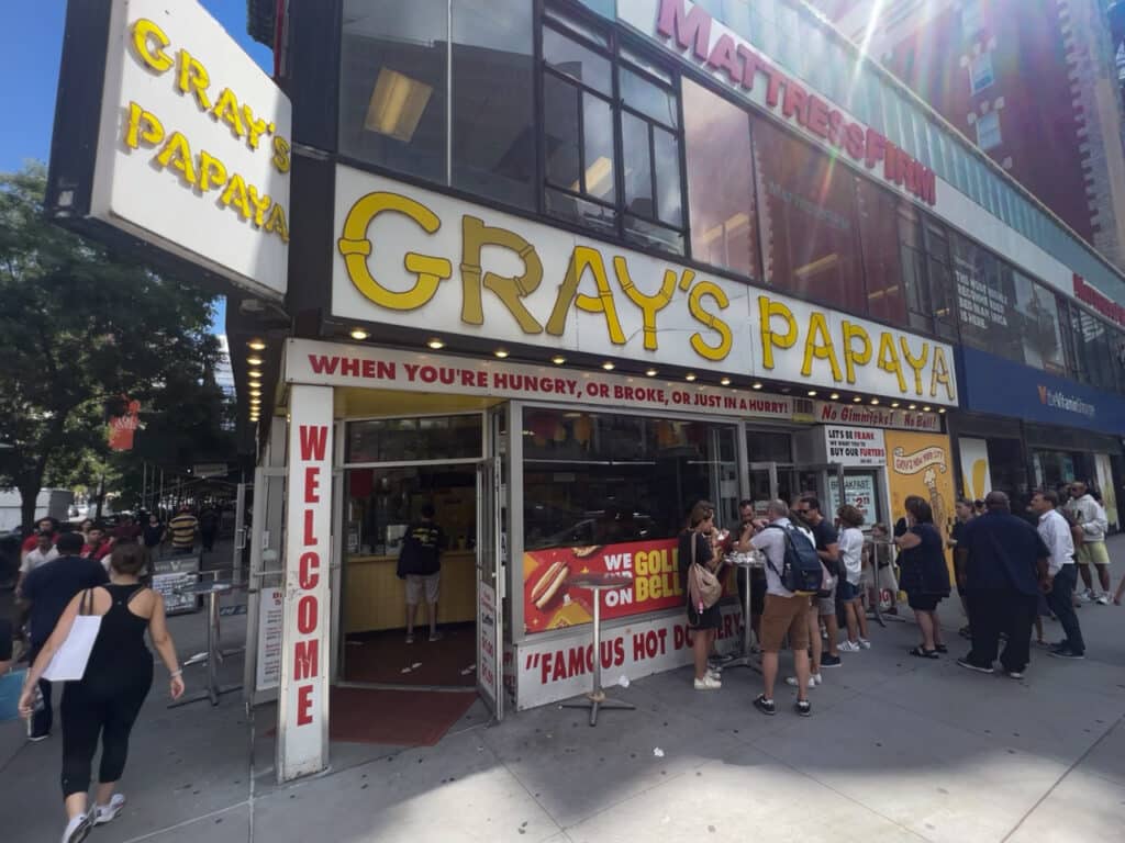 People waiting in line and eating hot dogs outside Gray's Papaya in New York City.
