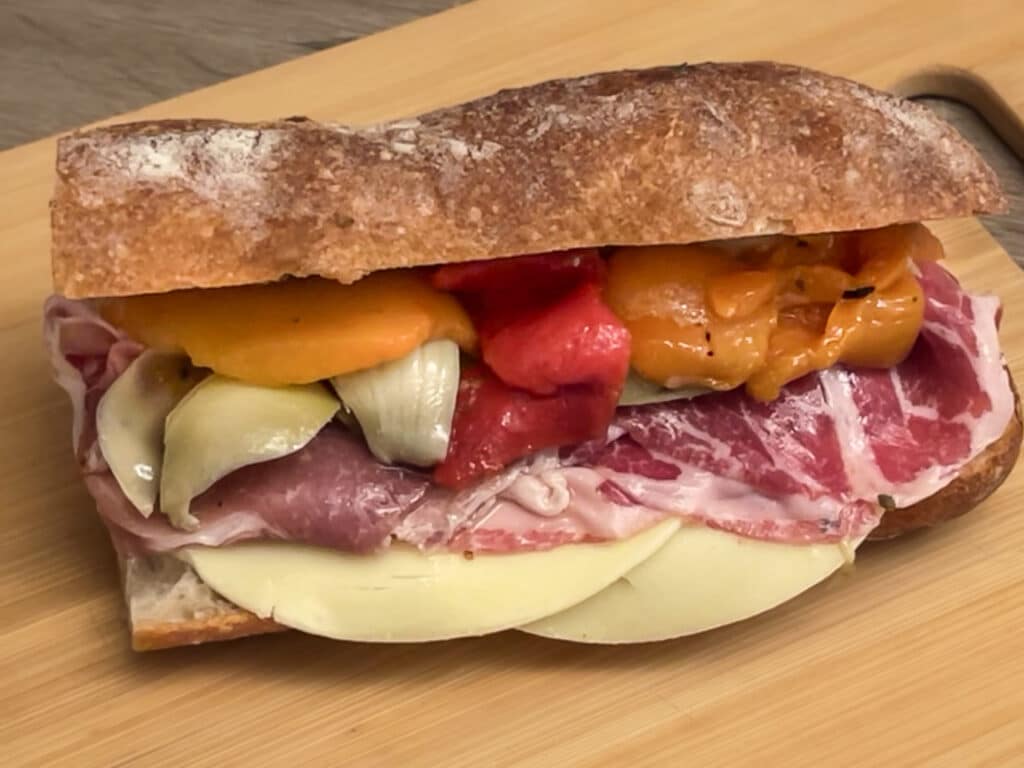 Sandwich on Italian bread made with prosciutto, capicola, cheese, roasted peppers, and marinated artichoke hearts. 
