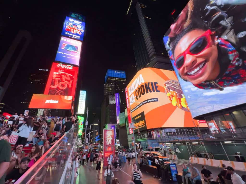 Crowds of people surrounded by large digital screens in Times Square, New York City at night.