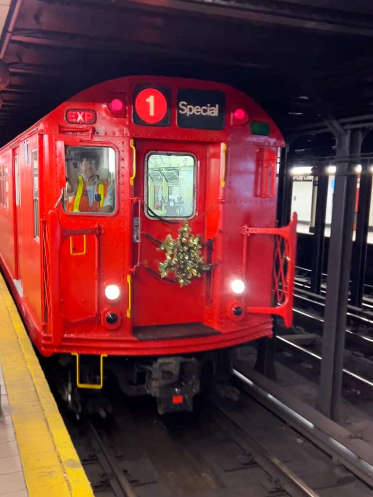 Red New York City Subway car with a Christmas wreathe decorating the front.