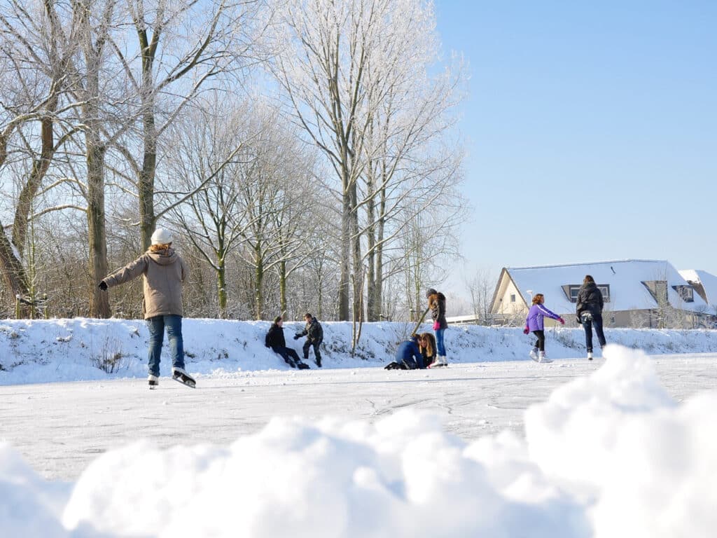 Small group of people ice skating on an outdoor pond that is surrounded by snow.