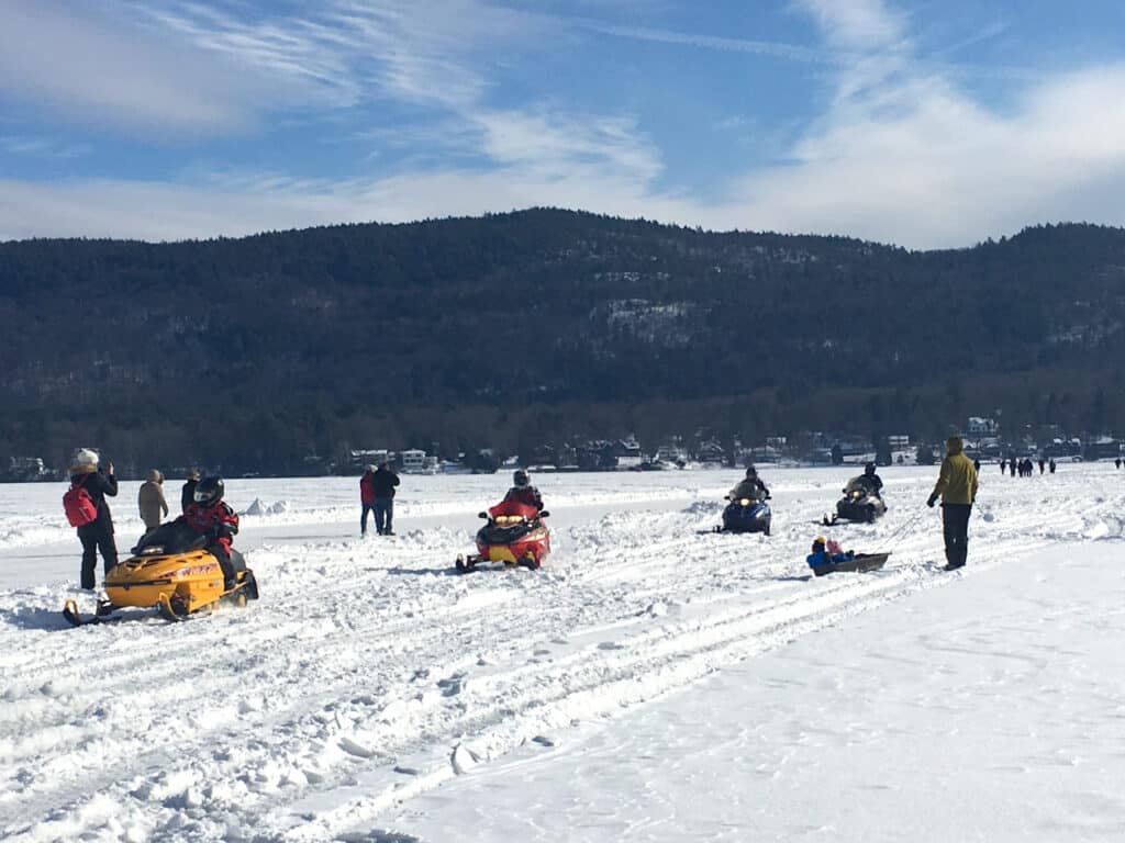 Snowmobilers riding on a frozen, snow-covered lake.