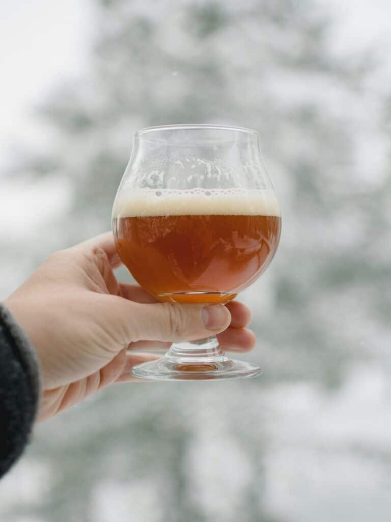 A person's hand holding a draft beer against a blurred snowy background.